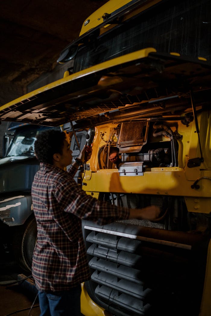 services-01 A mechanic works on a truck engine in a dimly lit garage, focusing on repairs.