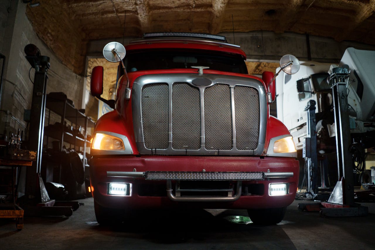 heros-img Front view of a red truck in a dimly lit automotive repair shop with a focus on the grill and headlights.