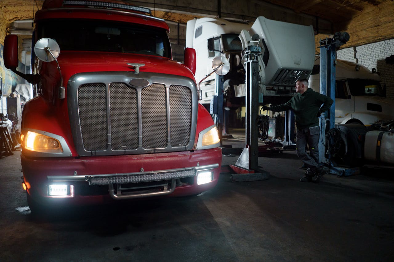 services-03 Red truck in a garage with mechanic and elevated vehicles undergoing maintenance.