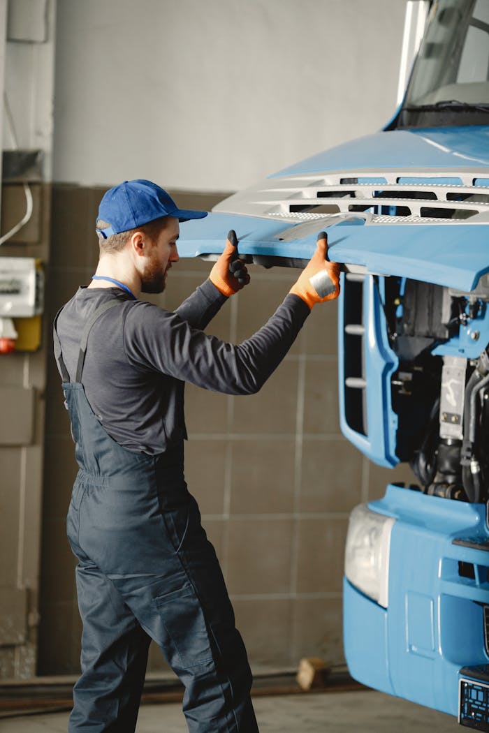 our-story Mechanic in overalls fixing the front of a blue truck in a workshop garage.