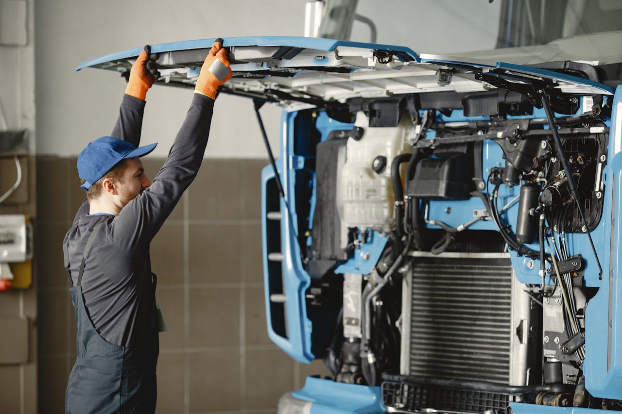 about-us Mechanic in uniform inspecting truck engine for maintenance indoors.